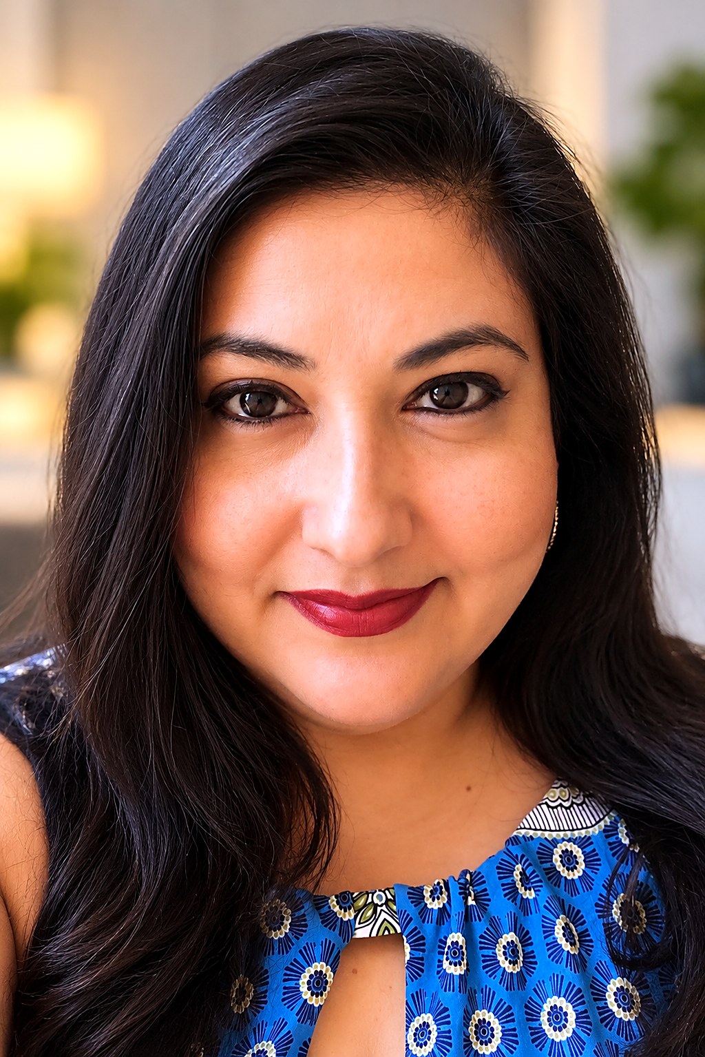 Andrea J. Lopez smiling warmly in a blue patterned top, in a softly lit room